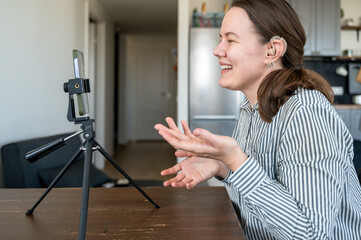 Portrait of young smiling woman with hearing aid on left ear recording video or making video call...