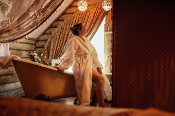 A young woman in a white bathrobe in the hotel bathroom. A charming girl is going to take a bath and enjoy a spa procedure.