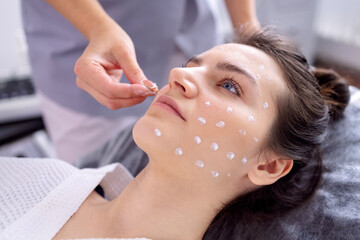 Close up of beautician applies ampoule cream to face of female client in spa salon