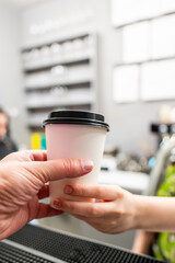 A close-up of a handover of a takeaway coffee cup at a modern cafe counter, capturing the exchange and hospitality