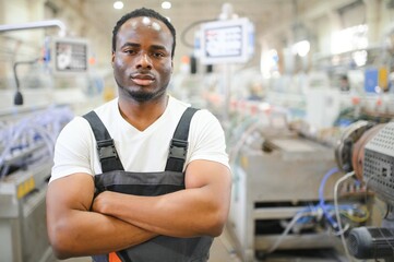 African male engineer. Control a material production machine system, working in a plastic and steel...