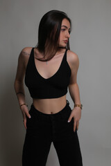 Naklejka premium Portrait of a beautiful fashion model in the studio on a light background, wearing a black short clothes and trousers, barefoot