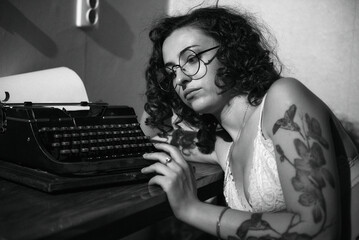 A girl with a tattoo sits near a typewriter and thinks about something. Grain effect used