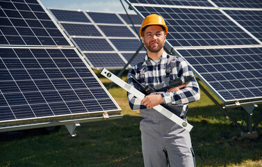 Portrait, holding leveler tool. Engineer with photovoltaic solar panels outdoors at daytime