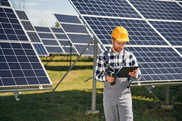 On the field with notepad in hands. Engineer with photovoltaic solar panels outdoors at daytime