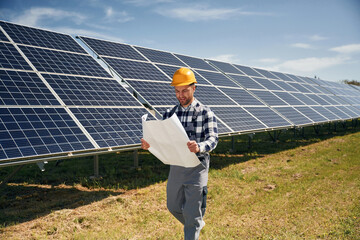 Big paper with plan, reading. Engineer with photovoltaic solar panels outdoors at daytime