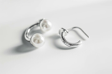 A pair of mismatched earrings, one a pearl stud and one a silver hoop, resting on a clean white background.