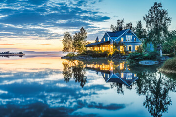 Fototapeta premium A serene waterfront property overlooking a tranquil lake, its pristine facade mirrored in the calm waters at sunrise.