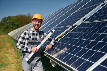 Obraz premium Portrait, holding leveler tool. Engineer with photovoltaic solar panels outdoors at daytime