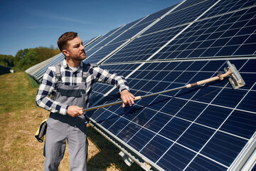 Mop in hands. Cleans the surface. Engineer with photovoltaic solar panels outdoors at daytime