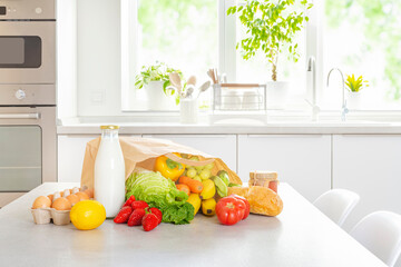 Various healthy food from paper bag on table with kitchen window interior background