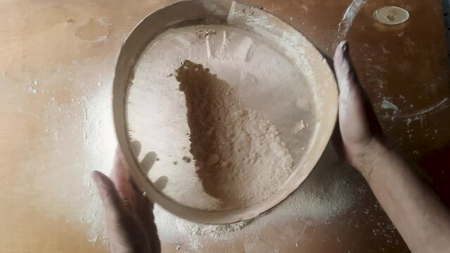 Woman sifting flour with wooden sieve, close-up
