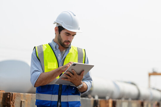 Heavy-duty industrial engineers stand in a pipeline manufacturing facility using digital tablet computers for the construction of products to transport oil, gas and fuel.