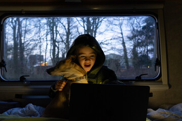 Boy with his dog looking at the computer inside a motorhome at night