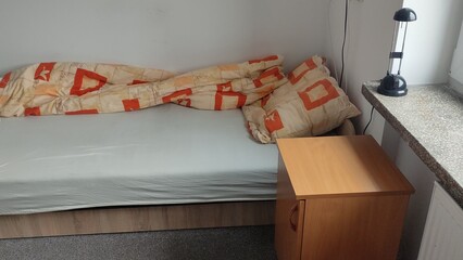 Unmade bed and room in a student dormitory or inexpensive hostel. Minimalistic room interior