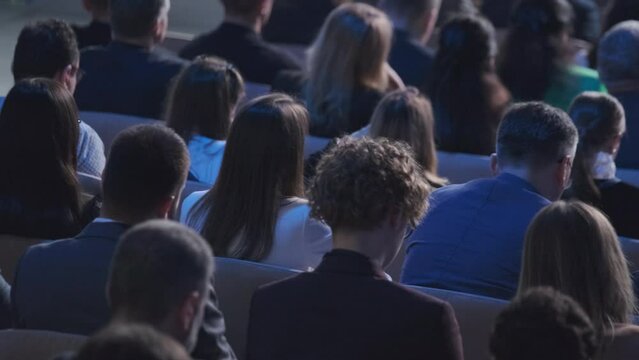 A diverse group of attendees at a conference, captured from behind, focused on a presentation. The image portrays engagement and professional development in a corporate setting.