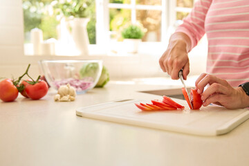 Close Up Of Woman At Home Preparing Meal In Kitchen Slicing Tomato On Chopping Board