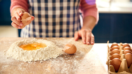 Close Up Of Woman At Home In Kitchen Adding Eggs To Flour Making Dough On Worktop Or Counter
