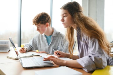students sit at shared desk making notes studying together at university