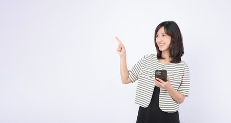 Asian woman is holding a mobile phone and pointing to an empty space on a white background.