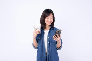 Asian woman wearing denim jean is holding dollar and a mobile phone against a white background,...