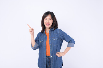 A Young asian woman wearing orange t shirt and denim jean while pointing finger to free copy space isolated on white studio background