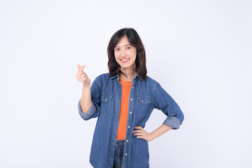 Asian woman wearing orange t shirt and denim jean is making a mini heart gesture on a white background.