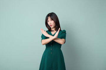 asian woman green dress showing denied gesture of X arm isolated on green background.