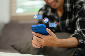 Happy young man using social media apps on smartphone sitting on couch at home