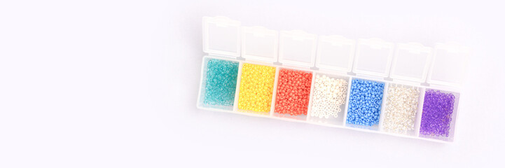 Multicolored beads in a storage container on a blue background. Banner with copy space.