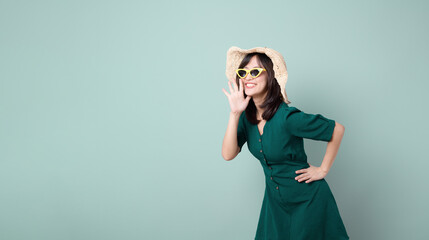 Happy Asian woman with sun glasses shouting above green dress poses against green background blank copy space for advertising content promotion