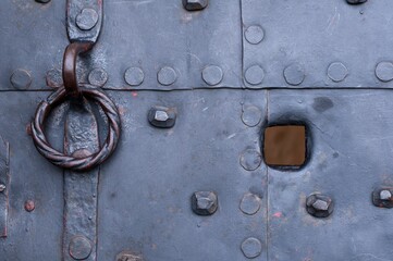 Old door covered with metal plates, painted gray, with a door knocker and a view hole, in Germany