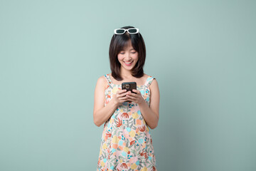Happy Asian woman using a mobile phone isolated on pastel green background.