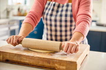 Close Up Of Woman At Home In Kitchen Rolling Out Dough With Rolling Pin On Worktop Or Counter