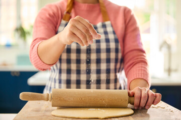 Close Up Of Woman At Home In Kitchen Sprinkling Flour On Rolled Out Dough On Worktop Or Counter
