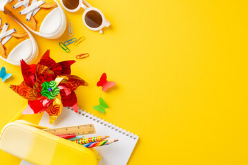 Bright and playful flat lay of children's summer school supplies, including a pinwheel, sneakers, and a notebook on a vibrant yellow backdrop