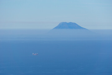 Distant Stromboli volcano with blue sea and sky on a hazy sunny day seen from Palmi, Calabria, Italy