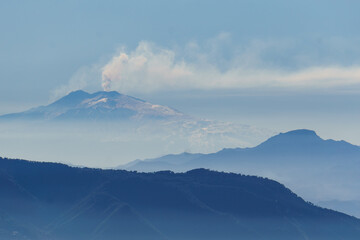Smoke rising up from active Etna volcano at Sicily on a hazy blue day seen from Palmi, Calabria, Italy
