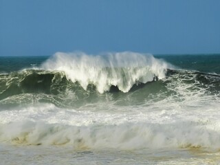 waves in the ocean with people standing near it and in the water