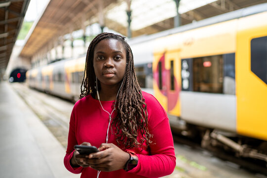 Black woman waiting at train station using smartphone