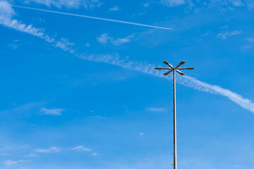 Vertical metal mast with lighting lanterns against a background of blue sky with light clouds.