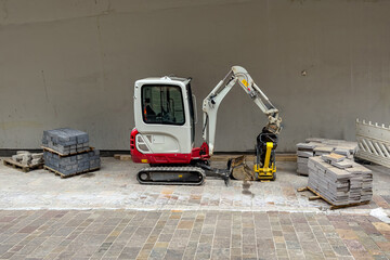 Small excavator on a construction site. Concrete paving slabs on wooden pallets.