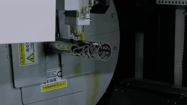 Automatic cnc laser cutting machine is working on cylindrical metal workpiece with many sparks at factory, plant. Manufacturing, metalworking, industrial, and technology concept