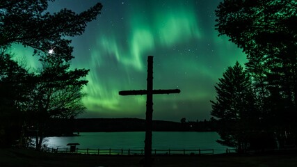 Naklejka premium Wooden cross is situated on the side of a road, with northern lights in the background