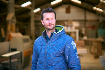 Portrait Of Carpenter Working In Woodwork Workshop Standing In Front Of Machinery