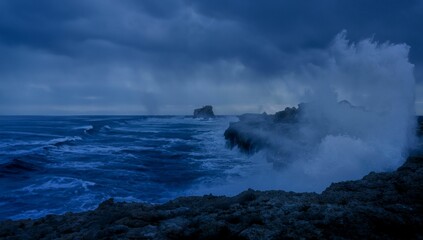 a crashing wave on the rocks of a shore line under a dark sky