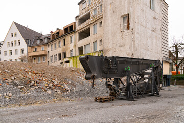 Part of a large machine near a pile of rubble from a destroyed building. Residential buildings...