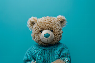 A whimsical photo of a cute teddy bear wearing a blue sweater on a solid teal background