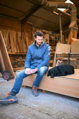 Carpenter Working In Woodwork Workshop With Pet Dog On Coffee Break