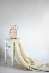 white chair with beige cloth on top and pitcher on white chair